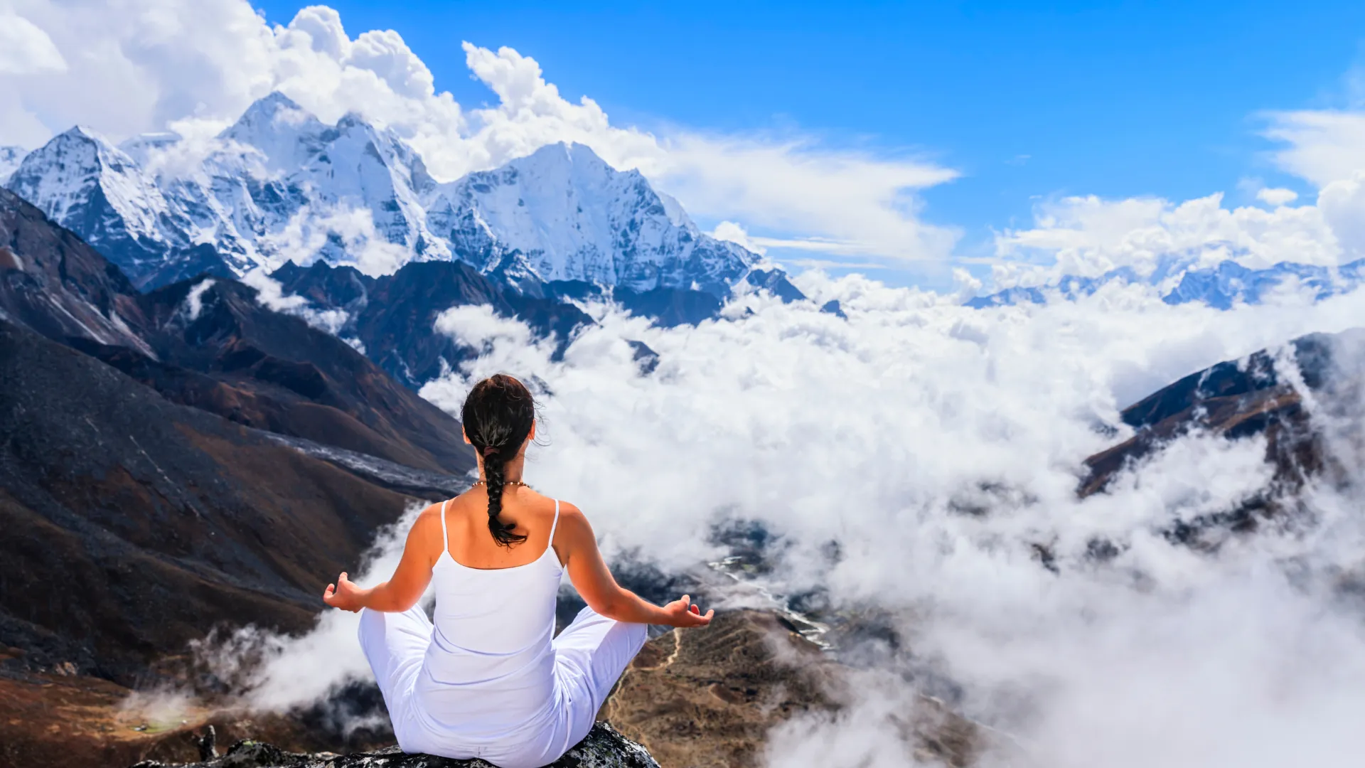 Una donna medita in posizione del loto sopra un mare di nuvole, davanti alle vette innevate dell'Himalaya